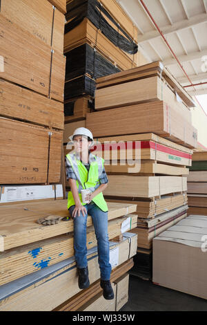 Female industrial worker having coffee while sitting on stack of wooden planks Stock Photo