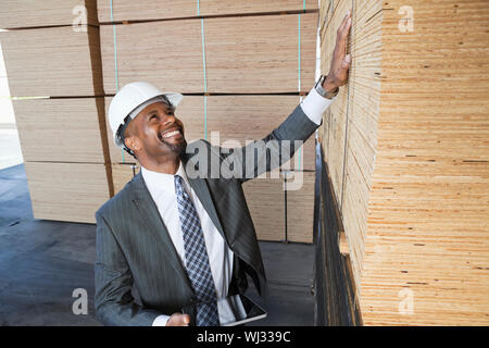 Happy African American male contractor inspecting wooden planks while holding tablet PC Stock Photo
