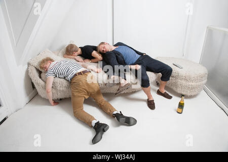 Drunk male friends sleeping on fur sofa after party Stock Photo