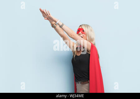 Young woman in superhero outfit pretending to leap in the air against light blue background Stock Photo