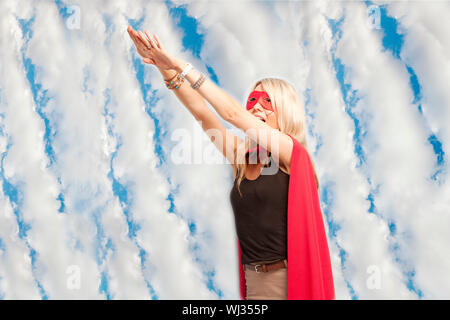 Young woman in superhero outfit taking a leap in the air against cloudy sky Stock Photo