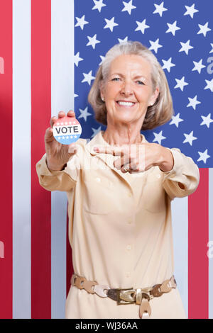 Portrait of senior woman pointing at election badge against American flag Stock Photo