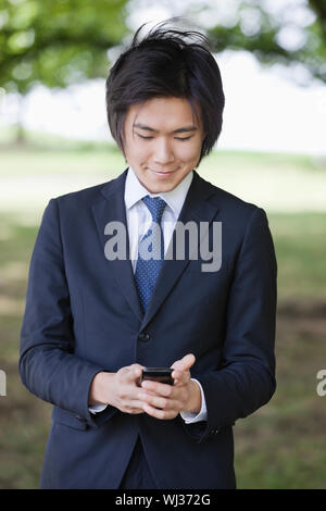 Young businessman using cell phone at park Stock Photo