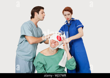 Male doctor with female nurse bandaging an injured patient against gray background Stock Photo