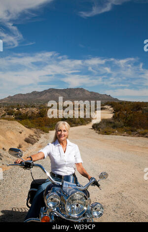 Senior woman riding motorcycle on desert road Stock Photo