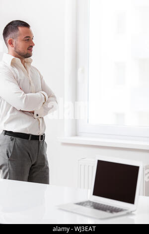 Businessman staring out of window with laptop in foreground Stock Photo