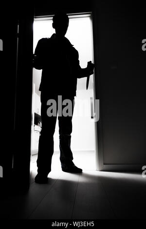 Full-length of thief with knife entering into dark room Stock Photo