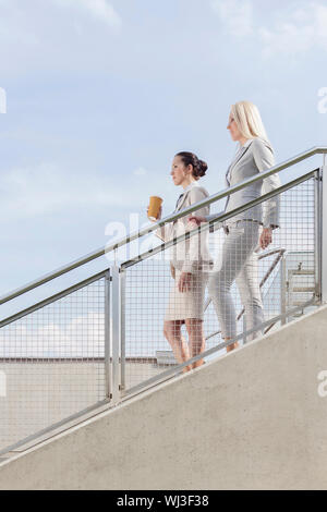 Side view of businesswomen moving down stairs against sky Stock Photo