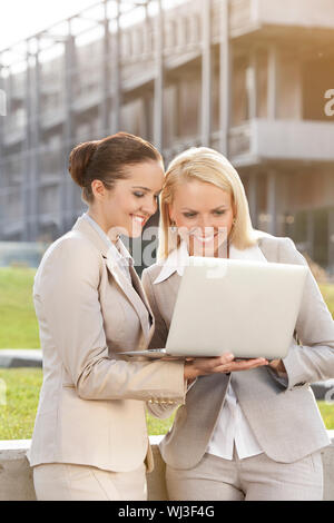 Happy young businesswomen using laptop together against building Stock Photo