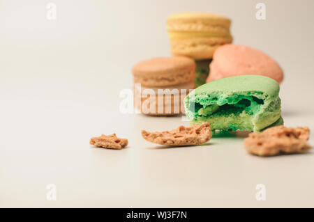 one green macaroon in the foreground lies a bite. Nearby are crumbs from a French pastry. In the background, three fresh colored macaroons lie in a pi Stock Photo