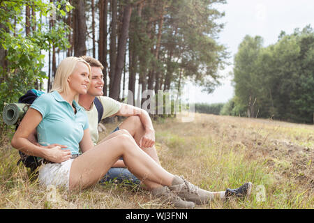 Thoughtful hiking couple looking away while relaxing in forest Stock Photo