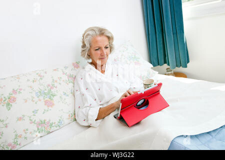 Senior woman using digital tablet on bed at home