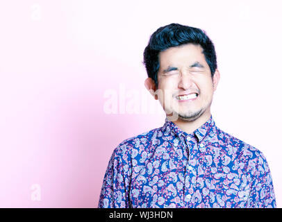 Young Geeky Asian Man in colorful shirt closing both eyes Stock Photo