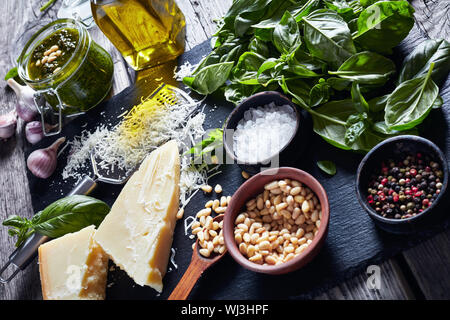 fresh basil leaves, grated parmesan cheese, pine nuts, garlic, peppercorns, bottle of olive oil on a rustic wooden table with homemade Basil pesto sau Stock Photo