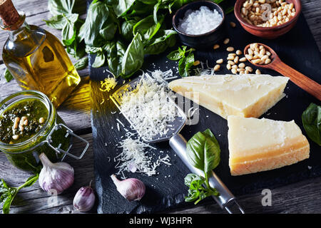 homemade Basil pesto sauce in a glass jar. fresh basil leaves, grated parmesan cheese, pine nuts, garlic, peppercorns in a bowl on a rustic wooden tab Stock Photo