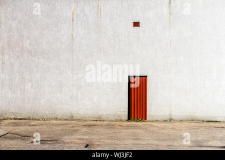 Red door in the middle of a gray concrete wall. Architecture background. Stock Photo