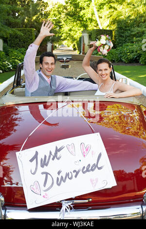 Happy couple in a convertible car waving with just divorced sign on it Stock Photo