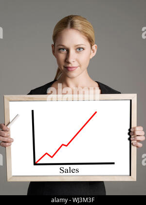 Portrait of young businesswoman showing sales graph against gray background Stock Photo