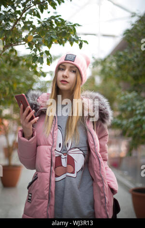 MINSK, BELARUS - January 19, 2019: A girl in a pink jacket walks with a telephone among the bushes in a building. Stock Photo