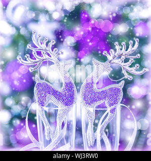 Two glass reindeer ornament on festive blurry background, Christmas tree with purple decoration, wine glasses, New Year greeting card Stock Photo