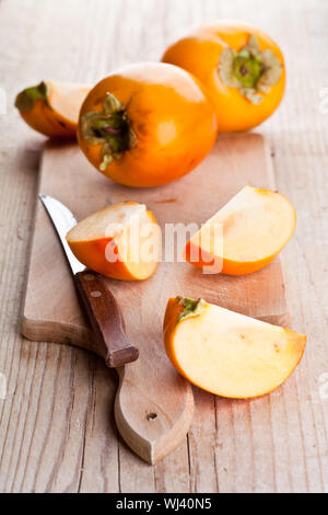 ripe persimmons and knife on wooden board Stock Photo