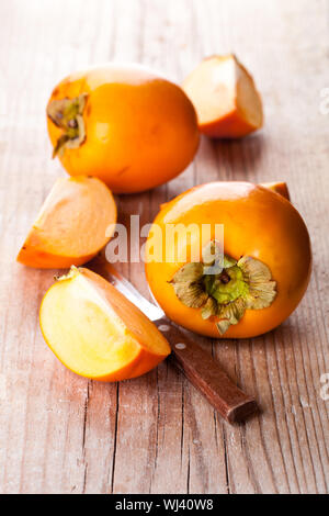 fresh sliced persimmons and knife on wooden background Stock Photo