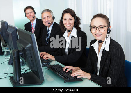 Line of professional stylish call centre operators wearing headsets seated behind their computers giving assistance Stock Photo