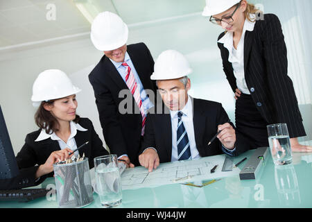 Meeting of four diverse architects or structural engineers in hardhats and suits seated in an office Stock Photo