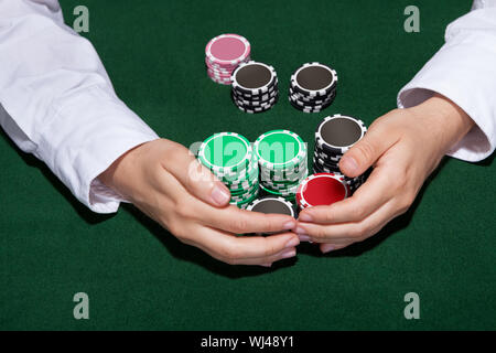 Croupier collecting in the bets at a casino table with his hands encircling various stacks of tokens or chips Stock Photo