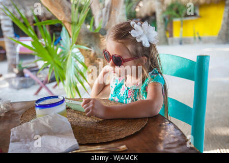 Little girl sitting in chair at restaurant waiting for her food Stock Photo