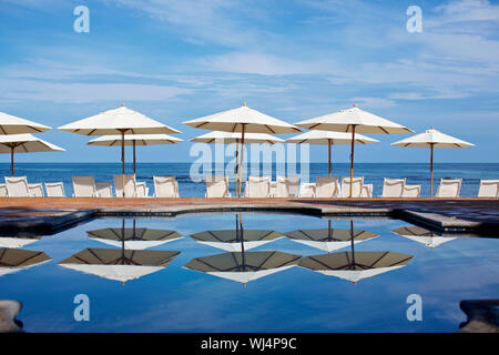 White beach umbrellas and lounge chairs at sunny ocean poolside, Punta de Mita, Nayarit, Mexico Stock Photo