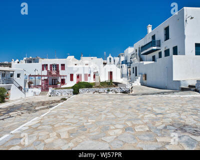 Ancient stone square surrounded by white houses against cloudless blue sky in town on Mykonos Island in Greece