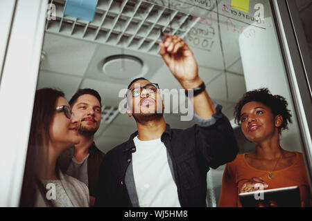 Portrait of a young businessman writing on a glass board explaining his concept to his colleague Stock Photo