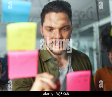 Portrait of a businessman brainstorming new startup business and writing on sticky notes stuck on transparent glass in office Stock Photo