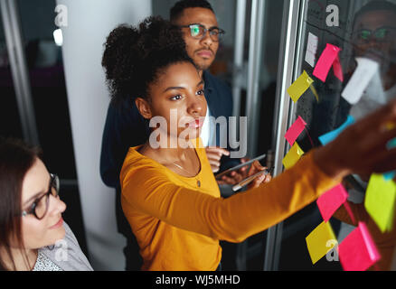 Business people in meeting brainstorming and discussing post it notes stuck on glass wall at office Stock Photo