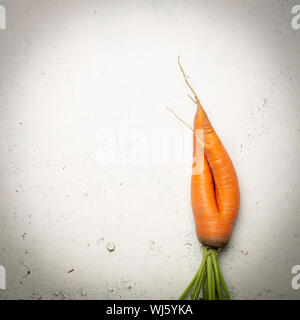 Ugly carrots on a white cracked surface. Ugly food concept, top view. Stock Photo