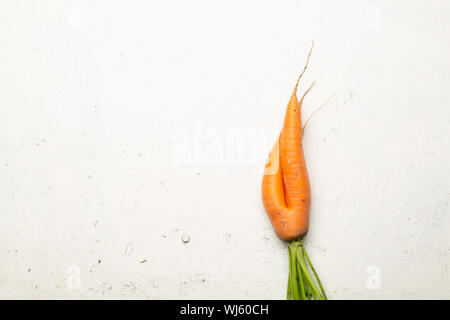 Ugly carrots on a white cracked surface. Ugly food concept, top view. Stock Photo