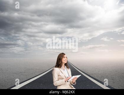 Composite image of businesswoman holding tablet and looking up standing on street under cloudy sky Stock Photo
