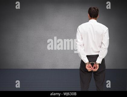 Composite image of young businessman wearing handcuffs in grey room Stock Photo