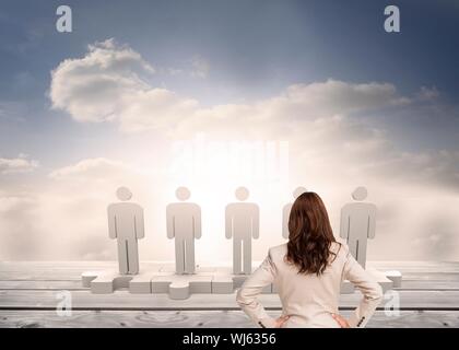 Composite image of businesswoman standing back to camera looking at 3d figure standing on puzzle in sky Stock Photo
