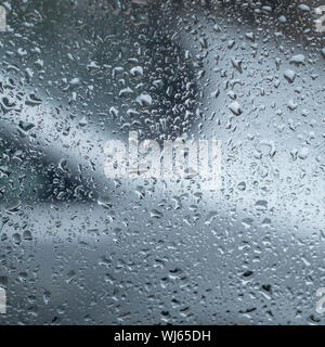 Raindrops on window glass with out of focus car in the background. Rain drops abstract, abstract water drops. Glass with water drops on it. Stock Photo