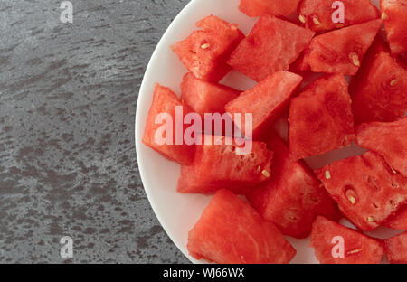 Top close view of a plate of watermelon chunks on a gray mottled table illuminated with natural lighting. Stock Photo