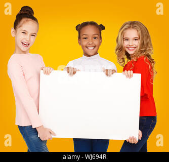 Happy multiracial girls holding blank banner, yellow background Stock Photo