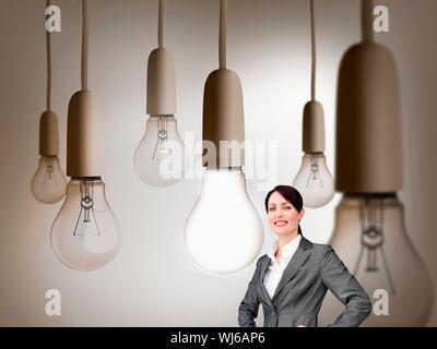 Composite image of attractive businesswoman standing in front of huge light bulbs Stock Photo