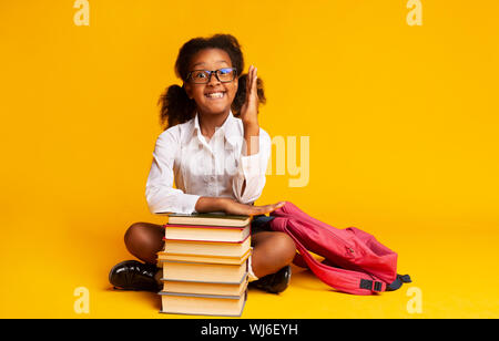 Black Elementary School Girl Raising Hand Sitting At Book Stack Stock Photo