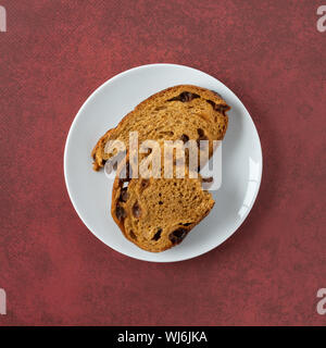 Top view of a pumpkin raisin bread slice broken in half on a white spotted plate atop a mottled maroon table illuminated with natural lighting. Stock Photo