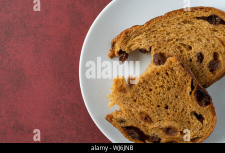 Top close view of a pumpkin raisin bread slice broken in half on a white spotted plate atop a mottled maroon table illuminated with natural lighting. Stock Photo