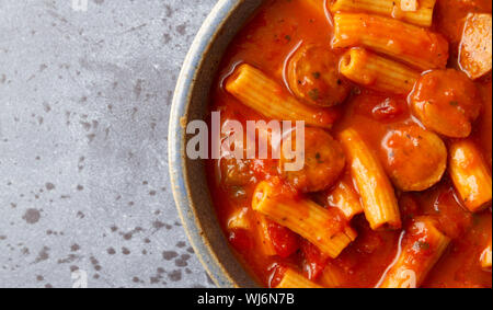 Top close view of rigatoni pasta and sausage in an old stoneware bowl on a gray background illuminated with natural lighting. Stock Photo