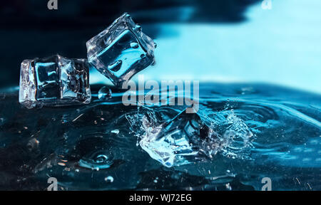 Ice cubes falling into the blue water. Splash of ice water. Water splashes from falling ice cubes. Stock Photo