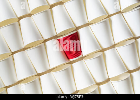 Background pattern of white coffee paper cups with red cup standing out in the middle. Diagonal orientation, copy space Stock Photo